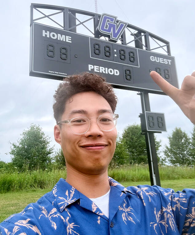 Hoan Lam Standing in front of the GVSU score board he programed
